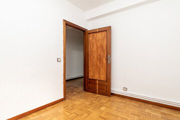 Empty living room with wooden door, oak parquet flooring and white painted walls