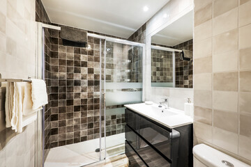 Bathroom with wall-mounted shower with marble tiles, square mirror on the wall and black cabinet...