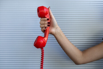 Red handset held by a woman's hand. Gray background. Vintage technology concept.