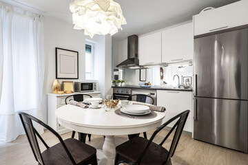 Round white dining table with food service next to kitchen of white wood cabinets with stainless steel appliances