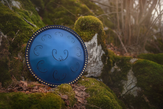 Musical instrument Rav Vast leaning against a mossy rock in the forest. Rav Vast is metal drum with perfectly cut steel tongues and a unique sound. 