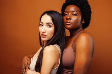 young pretty asian, african american woman posing cheerful together on brown background, lifestyle diverse nationality people concept