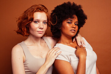 Obraz premium young pretty african and caucasian women posing cheerful together on brown background, lifestyle diverse nationality people concept