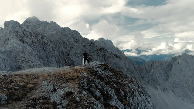 Aerial orbit of a couple on mountain peak of the panoramic mountaing range alps with a sky full of clouds - cinematic landscape drone shot