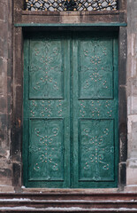 The old vintage green metal door on the facade of the baroque Dominican Cathedral in Lviv is decorated with decorative forged ornament. Snow lies on the stairs above the doorway.