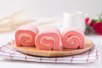 Pink strawberry roll cake or swiss roll with whipped cream and strawberry flavor on wooden plate