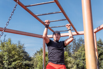 Latino man exercising arms crossing brachiation ladder outdoors