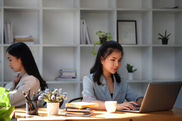 Obraz na płótnie Canvas Young asian business woman working with laptop computer while sitting with her colleague in office.