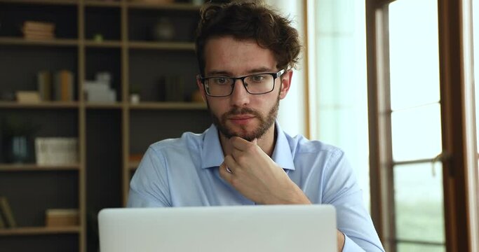 Thoughtful male worker in glasses sit at workplace look on pc screen consider on difficult work problem ponder on important question. Pensive young man doing project research contemplate on new idea