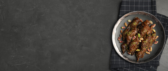 Delicious baklava with pistachio nuts and napkin on black table, top view. Space for text