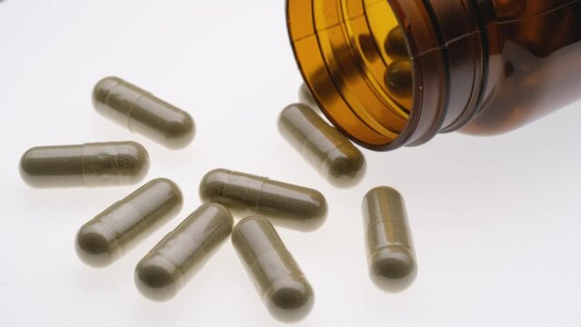 Herb capsule pill with brown bottle rotating on white background, Herbal medicine, Andrographis paniculata herbal, Top view and close up