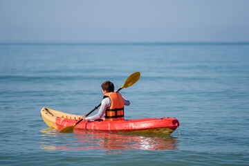 man in life jacket paddling a kayak boat in sea