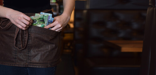 Female server using pockets of her apron to keep cash money tips web banner