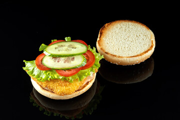 Burger with chicken cutlet, salad and mayonnaise. On a black mirrored background. The top bun is removed and lies next to it.