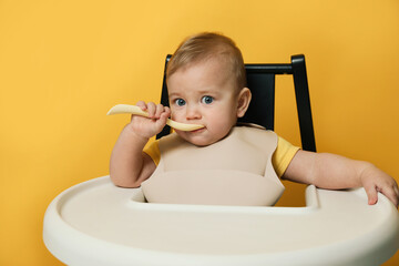 Cute little baby wearing bib while eating on yellow background