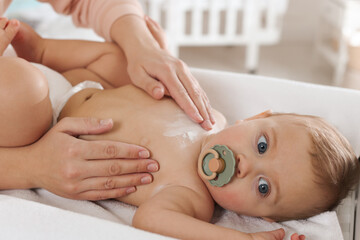 Mother applying dusting powder on her cute baby at home, closeup
