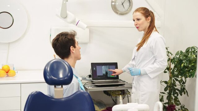 Female dentist showing dental x-ray on computer and explaining diagnose to male patient