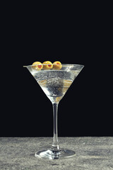 Martini cocktail with olives on grey table against dark background