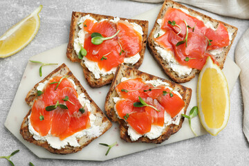 Delicious sandwiches with cream cheese, salmon and microgreens on light grey table, flat lay