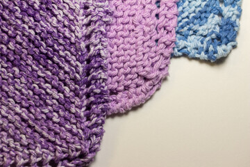 Macro abstract texture background of hand-knitted yarn wash cloths in a simple garter stitch, in varying shades of purple, pink and blue