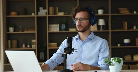 Young man in headphones sit at desk speak in condenser microphone record business podcast using audio editing app on laptop. Male remote employee address video conference talk to staff on web briefing