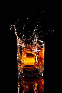 Scotch whiskey splash in glass with natural ice on black background.