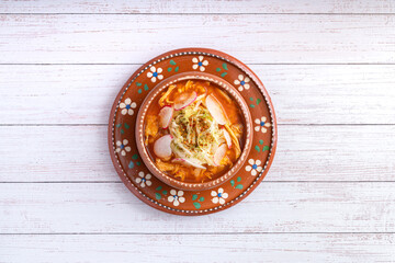 Traditional mexican food. Red pozole soup with chicken accompanied with avocado, lettuce, onion, radish, lemon, chili and crispy corn tortillas also known as tostadas on a white wooden background.