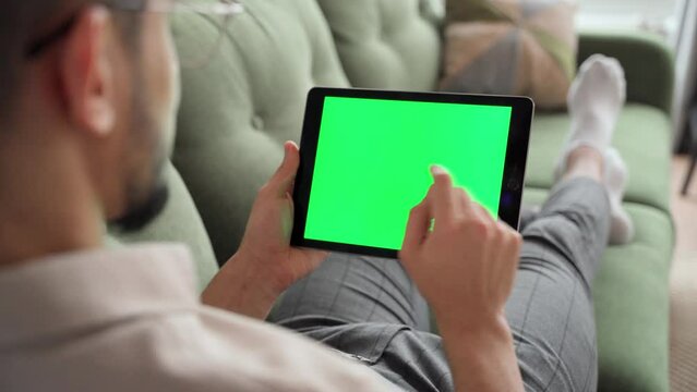 Rear view on green screen over shoulder man typing on tablet