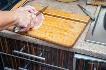 Cutting meat with a knife on a wooden board at home
