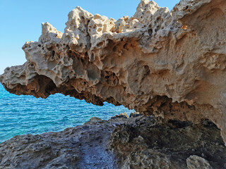 A stone, a rock, an overhanging piece of long-frozen lava, below dried salt, similar to ice, against the background of the sea and a blue cloudless sky.