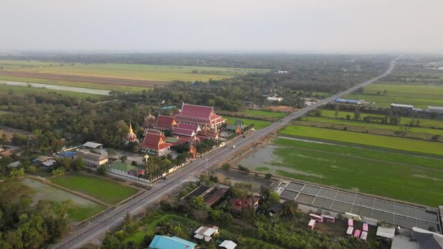 Aerial Drone Shot Hovering with Slight Tilt at a Thai Temple Along a Busy Road in Thailand.