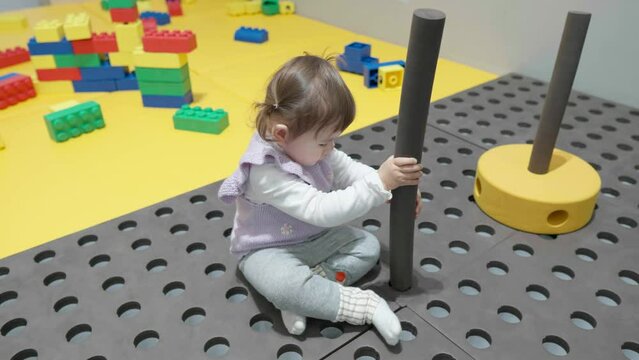 Little girl shove foam cylindrical stick into the floor hole in children's indoor playground