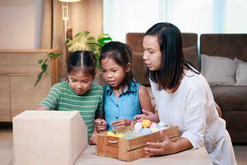 Asian mother and her daughters are decorating easter eggs preparing for Easter at home. Happy...