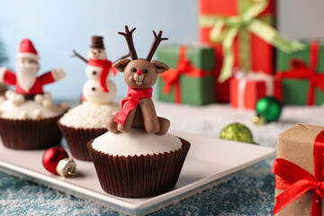 Different beautiful Christmas cupcakes on blue table with festive decor and snow