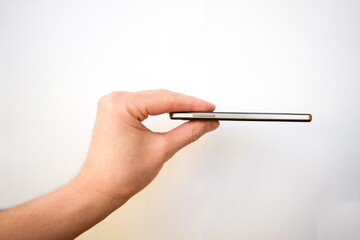 A man's hand holds a thin phone with his fingers on a white background