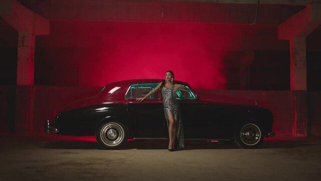 Beautiful Elegant Young Woman Standing , Dancing and Flirting near old retro classic car. Old fashioned luxury style concept . Rich fashion lifestyle . Luxury dress with fabric glitter, spangles .