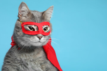Adorable cat in red superhero cape and mask on light blue background, space for text