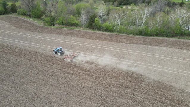 Overhead view of farmer discing field in preparation for planting. Creek on other side of line of trees. Dust clouds following the farmer. Rural housing development seen in the valley. 