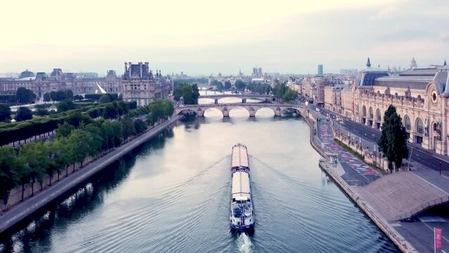 Aerial moving (back up) over Seine river, with a barge moving opposite. View on Louvre Museum, Notre-Dame in Background, Orsay. Paris, France