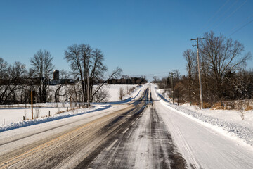 A straight road in the country, freshly plowed and salted after a snow fall.