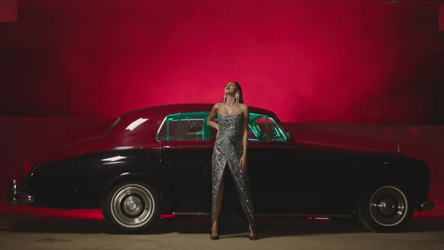 Beautiful Elegant Young Woman Standing , Dancing and Flirting near old retro classic car. Old fashioned luxury style concept . Rich fashion lifestyle . Luxury dress with fabric glitter, spangles .