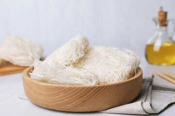 Wooden bowl with uncooked rice noodles on light table, closeup
