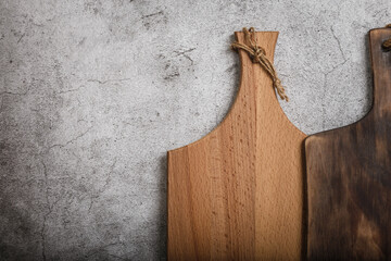 Samples of various handmade rustic wooden cutting boards on a kitchen countertop against a concrete wall background. Manufacture of household goods and accessories made of wood
