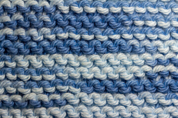 Macro abstract texture background of hand-knitted yarn fabric in a basic garter stitch, in varying shades of blue and white.