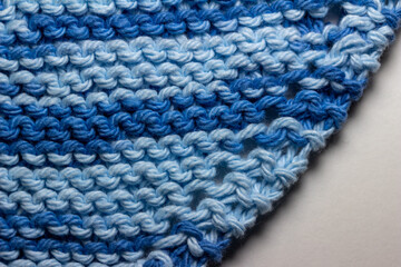 Macro abstract texture background of hand-knitted yarn fabric in a basic garter stitch, in varying shades of blue and white.