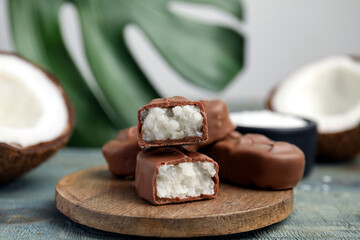Delicious milk chocolate candy bars with coconut filling on blue wooden table, closeup. Space for text