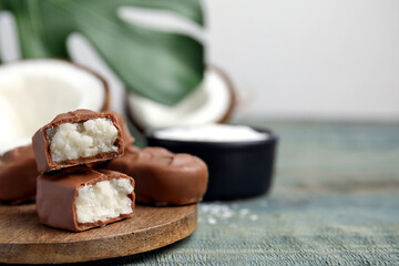 Delicious milk chocolate candy bars with coconut filling on blue wooden table, closeup. Space for text