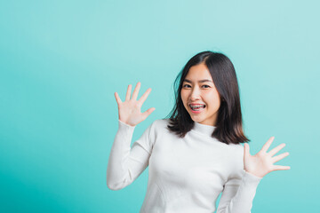 Fototapeta premium Young beautiful Asian woman cheerful smiling makeup showing open hands, Portrait happy female shocked she shows palms, studio shot isolated on a blue background