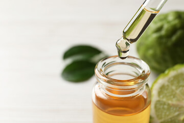 Dripping bergamot essential oil into glass bottle on table, closeup. Space for text