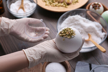 Woman in gloves making bath bomb at wooden table, closeup